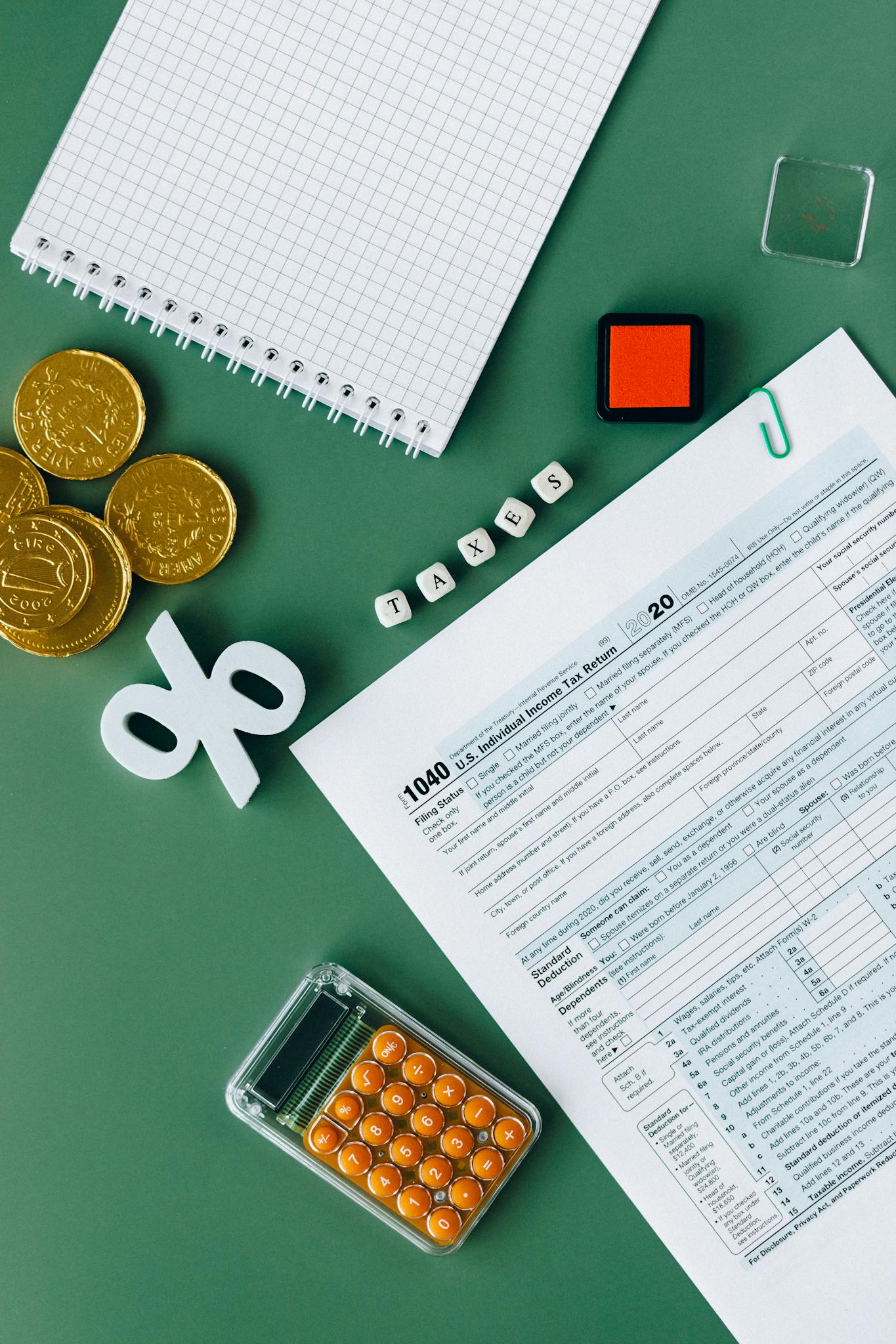 Tax documents and office supplies on green surface, indicating tax season planning and finance concepts.